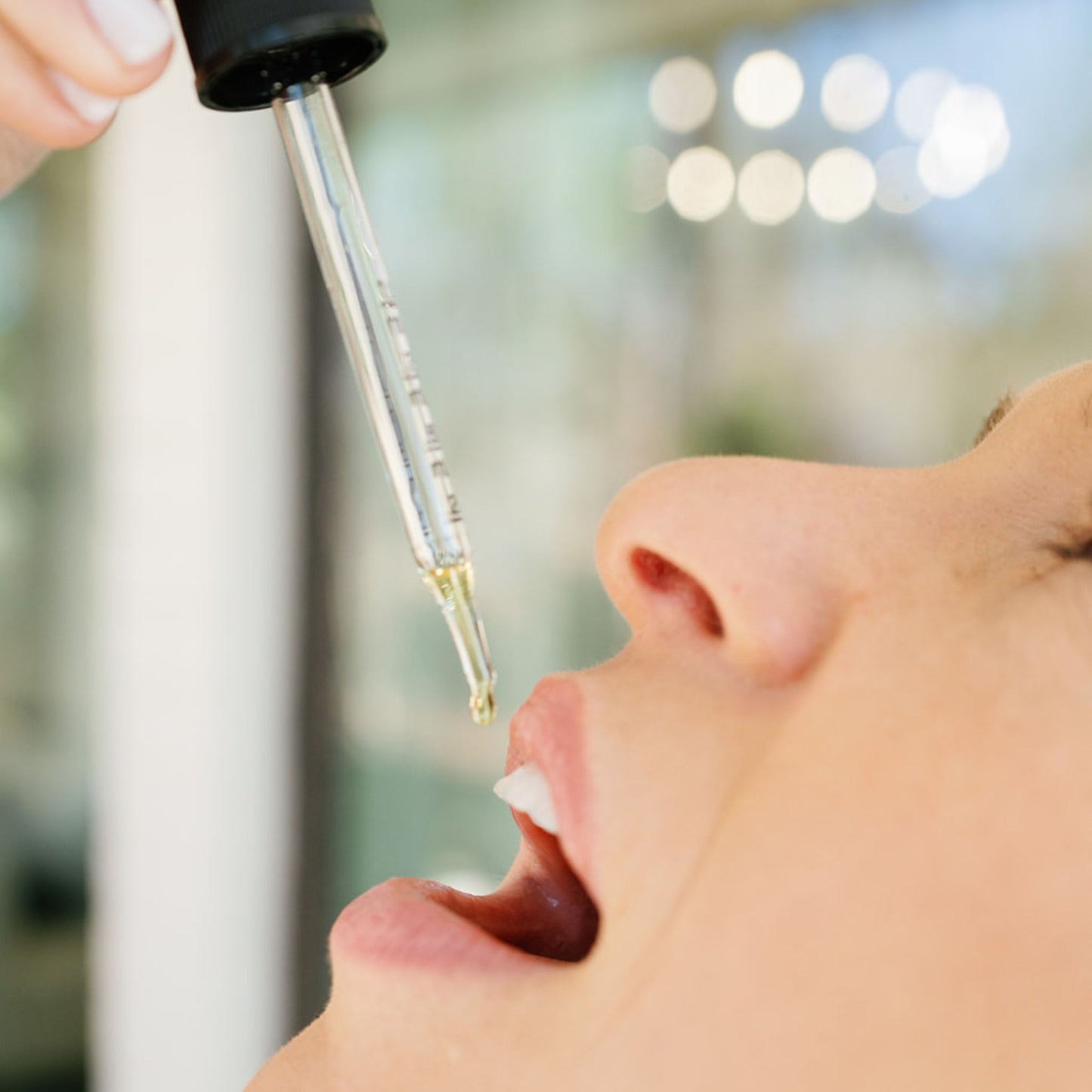 Euphrates tincture with oil being dropped into a womans mouth with white teeth visible and windows to a home behind her