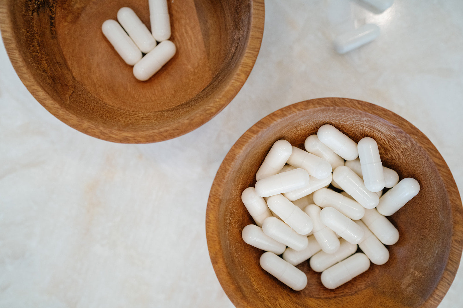 White capsules in two wooden bowls on granite counter top